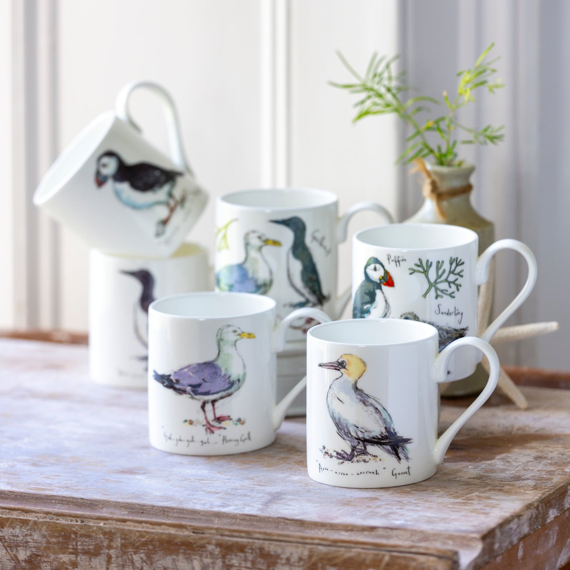 Set of mugs with bird illustrations on a wooden surface