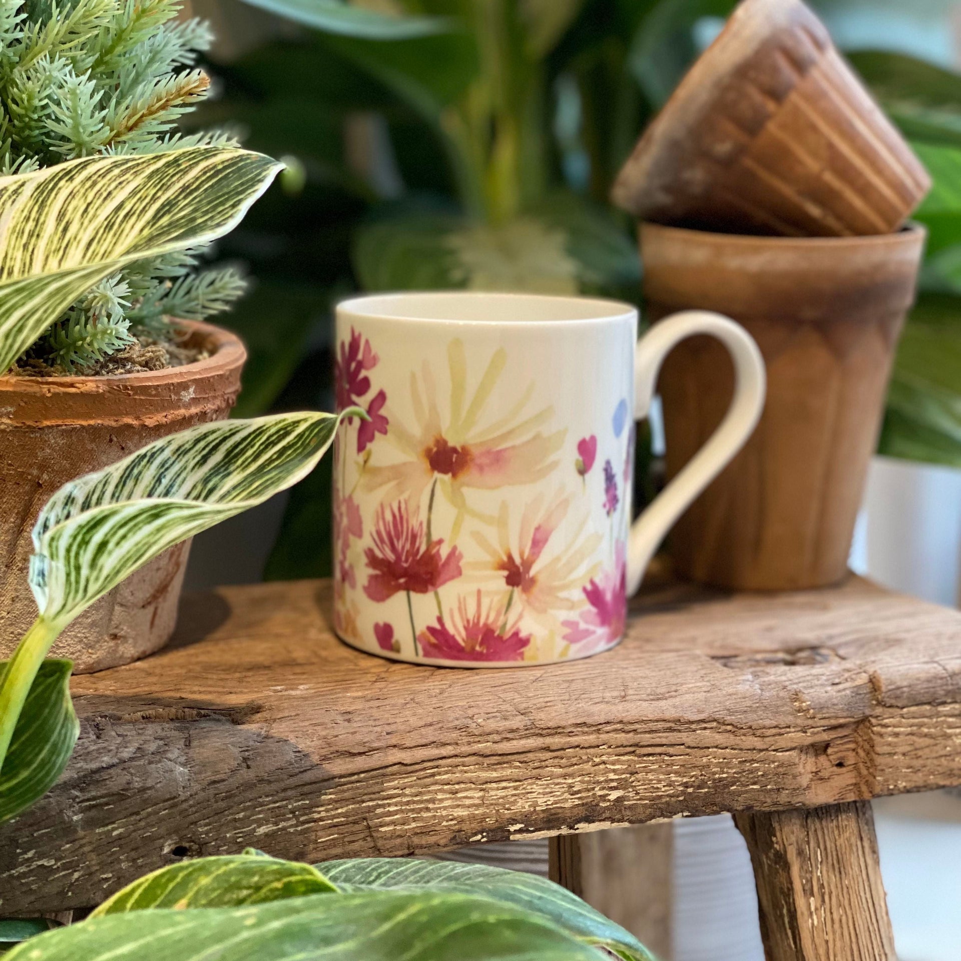 Mug with floral design on a wooden surface surrounded by plants