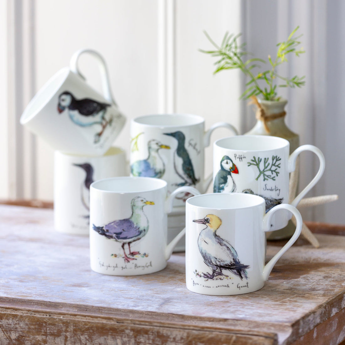 Set of mugs with bird illustrations on a wooden surface