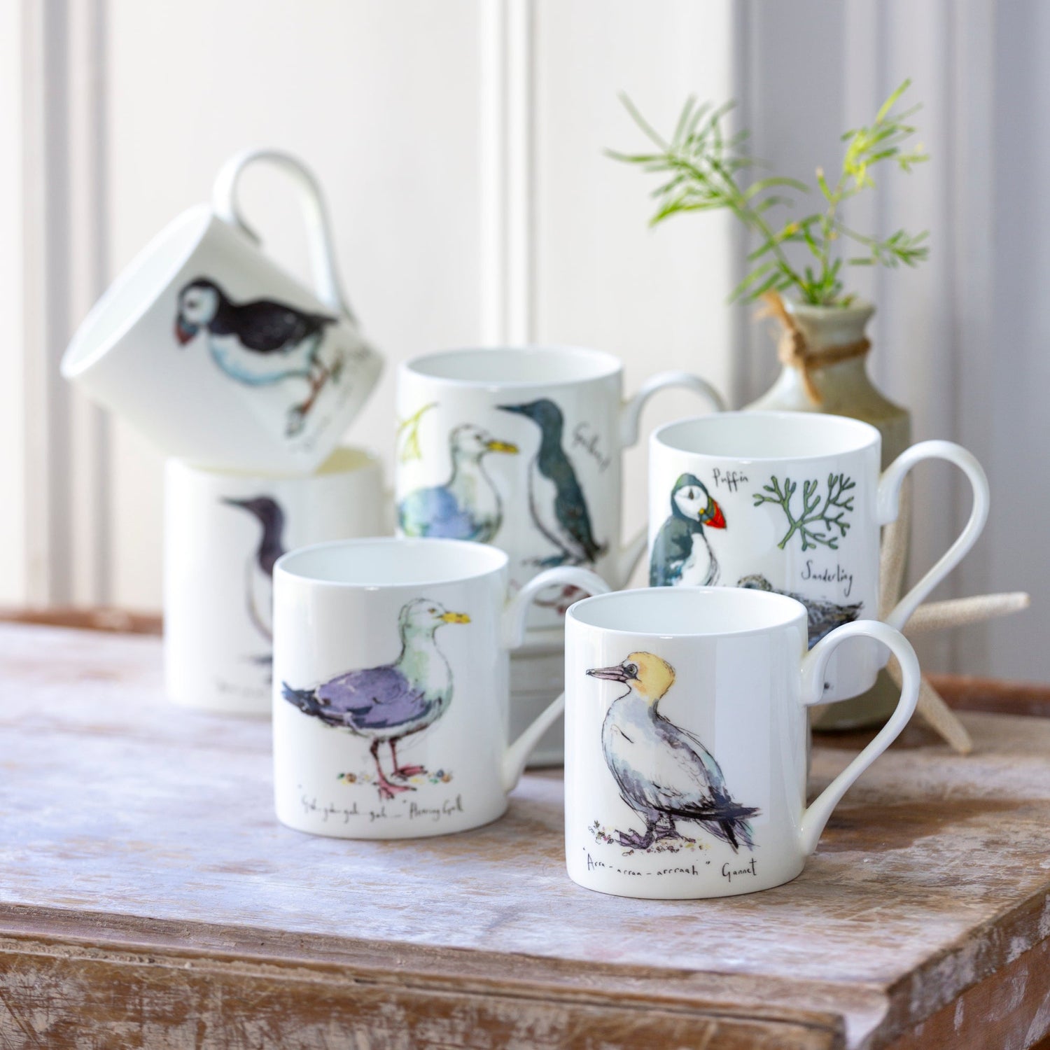 Set of mugs with bird illustrations on a wooden surface