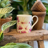 Mug with floral design on a wooden surface surrounded by plants