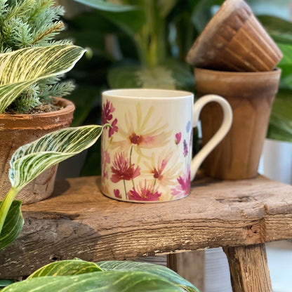 Mug with floral design on a wooden surface surrounded by plants