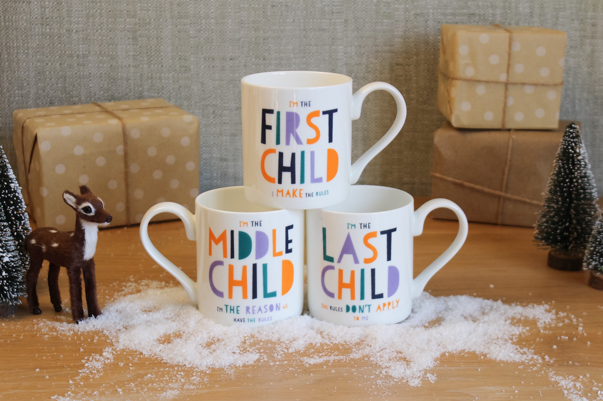 Three mugs with colorful text on a wooden surface with decorative items.