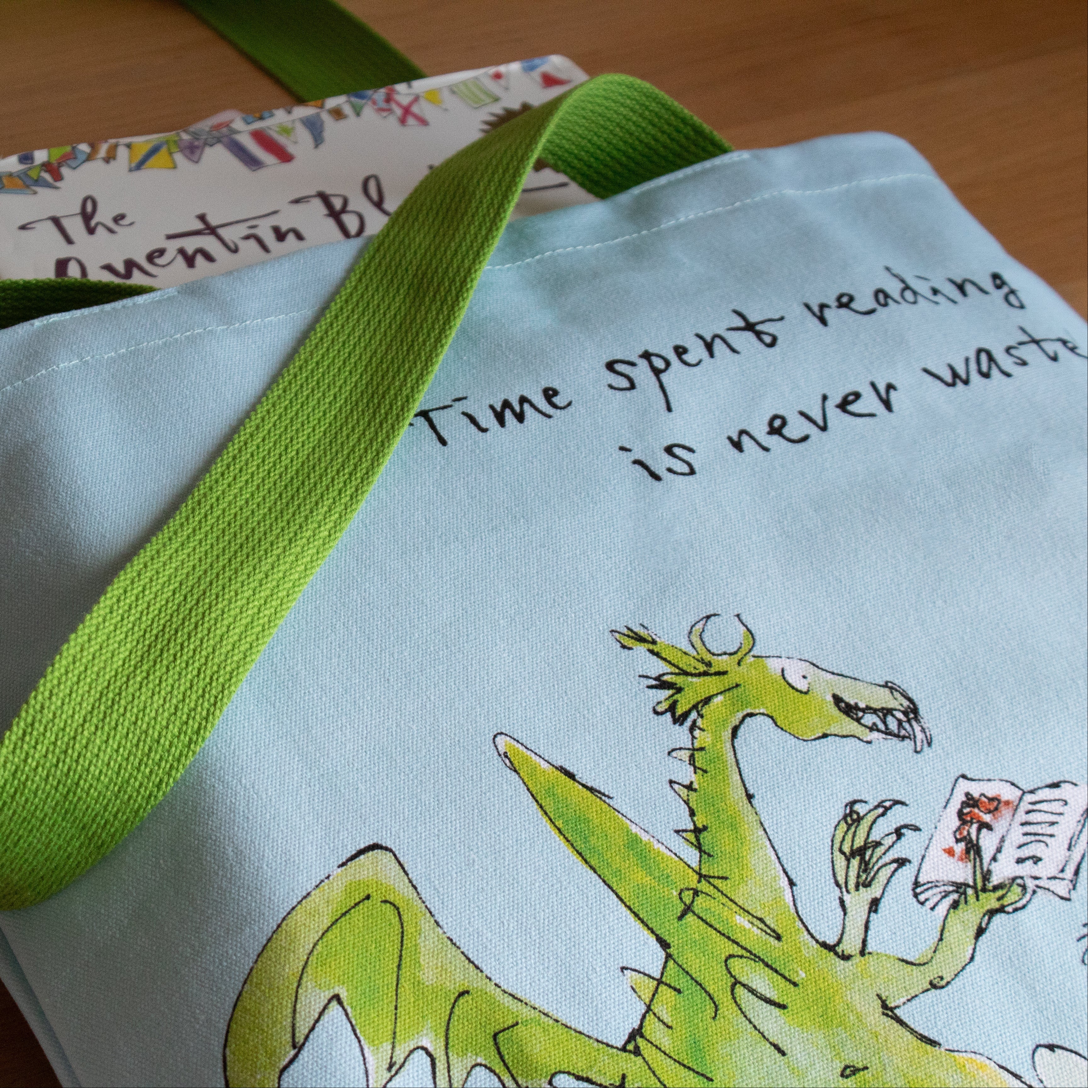 Tote bag with a dragon design and text, placed on a wooden surface with books underneath.