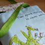 Tote bag with a dragon design and text, placed on a wooden surface with books underneath.