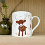 Mug with a reindeer design on a wooden surface with a thistle and vase in the background