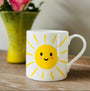 White mug with a sun design on a wooden surface with pink flowers in the background